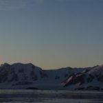 A sunset over a body of water with a mountain in the background.